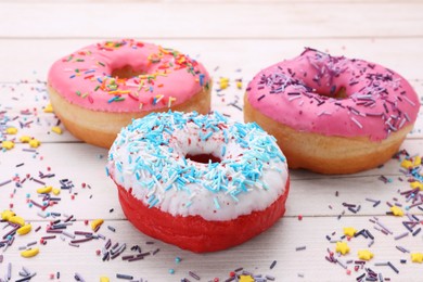 Photo of Glazed donuts decorated with sprinkles on white wooden table, closeup. Tasty confectionery
