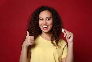 Photo of African-American woman with vitamin pill on red background