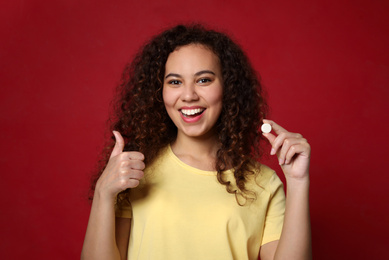 African-American woman with vitamin pill on red background