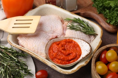 Photo of Fresh marinade, raw chicken, rosemary and tomatoes on brown table, closeup