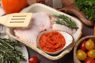 Fresh marinade, raw chicken, rosemary and tomatoes on brown table, closeup