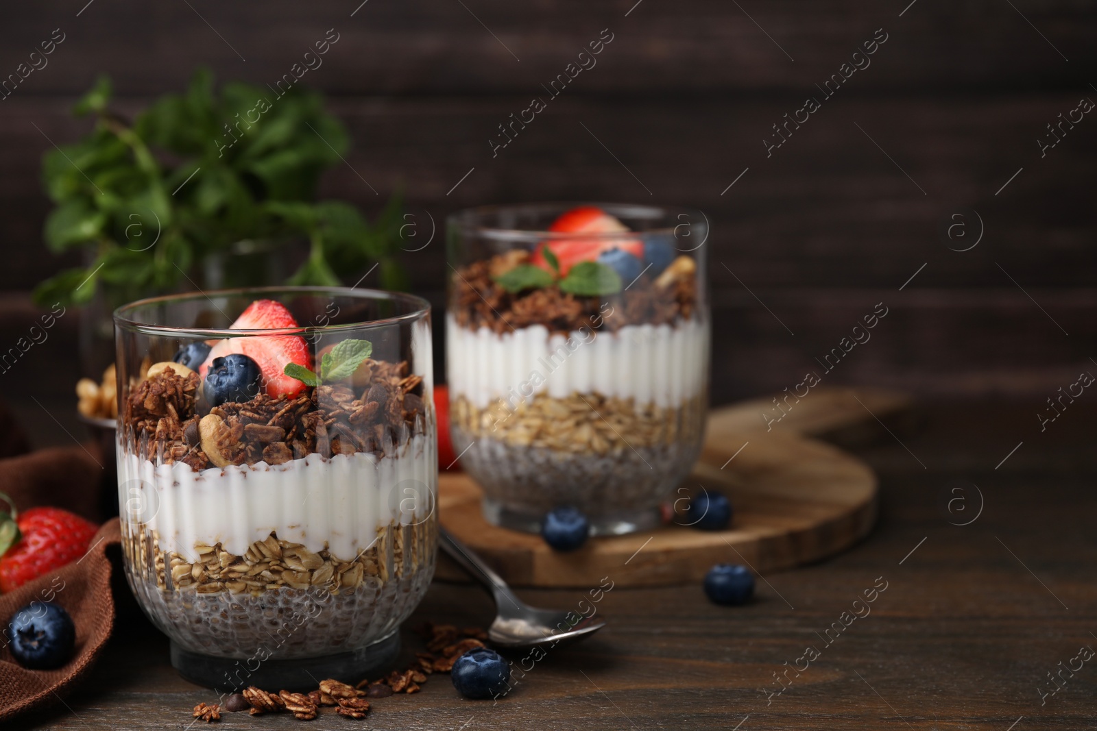 Photo of Tasty granola with berries, nuts, yogurt and chia seeds on wooden table, space for text