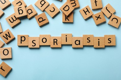 Photo of Word Psoriasis made of wooden squares with letters on light blue background, flat lay