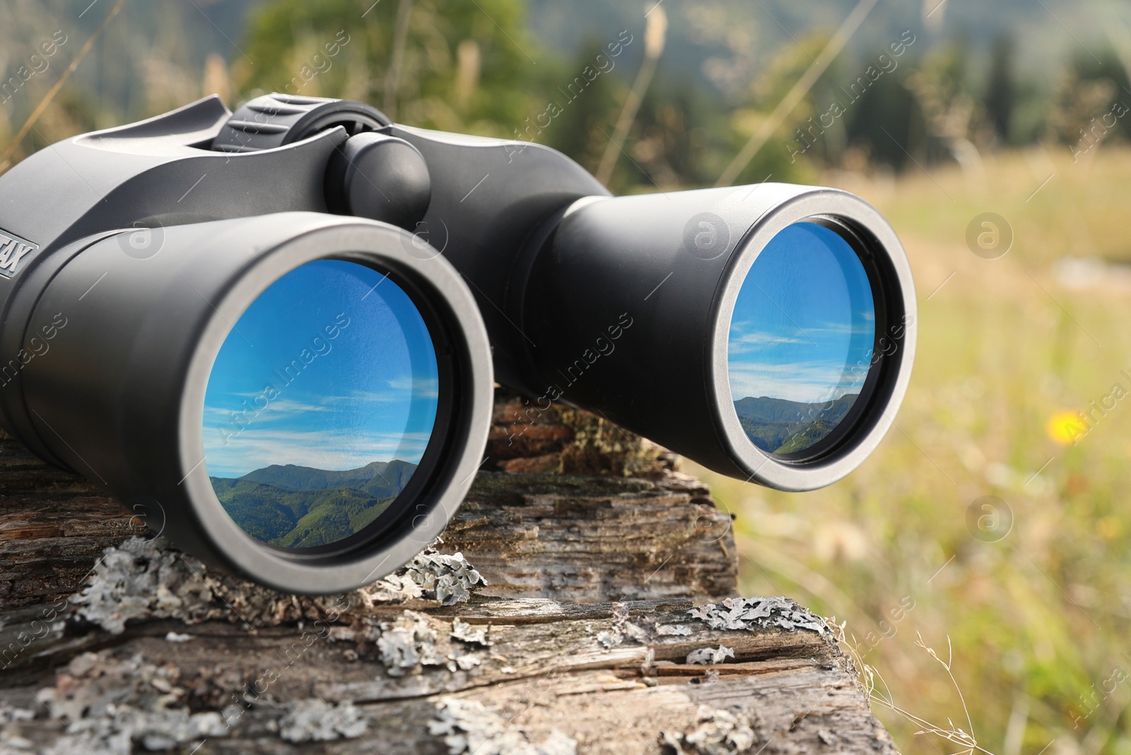 Image of Binoculars on wooden log outdoors, closeup. Mountain landscape reflecting in lenses