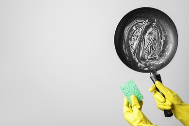 Woman holding dirty frying pan and sponge on white background, closeup. Space for text