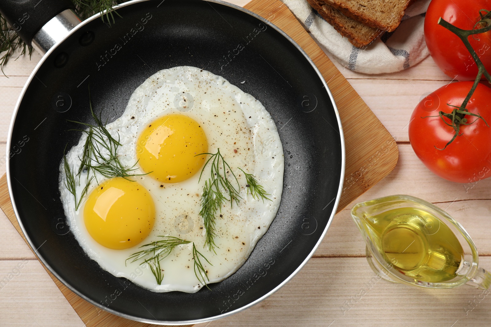 Photo of Frying pan with tasty cooked eggs and other products on light wooden table, flat lay