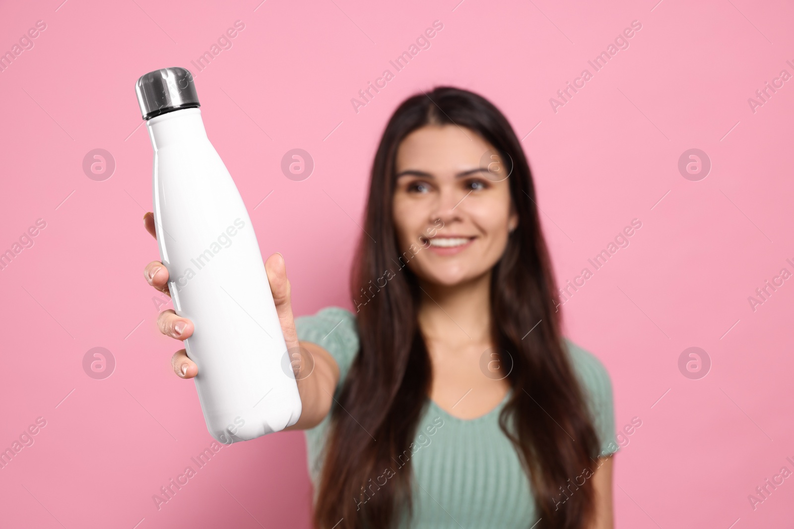 Photo of Young woman with thermo bottle against pink background, focus on hand