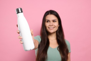 Young woman with thermo bottle against pink background, focus on hand