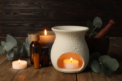 Photo of Aromatherapy. Scented candles, bottles and eucalyptus branches on wooden table, closeup