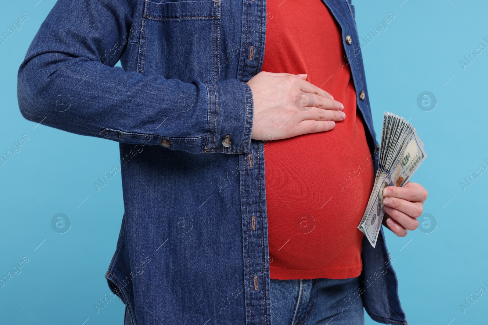 Photo of Surrogate mother. Pregnant woman with dollar banknotes on light blue background, closeup