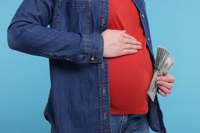 Photo of Surrogate mother. Pregnant woman with dollar banknotes on light blue background, closeup