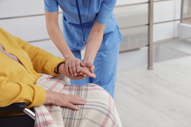 Nurse massaging hand of senior woman in wheelchair at hospital, closeup. Medical assisting