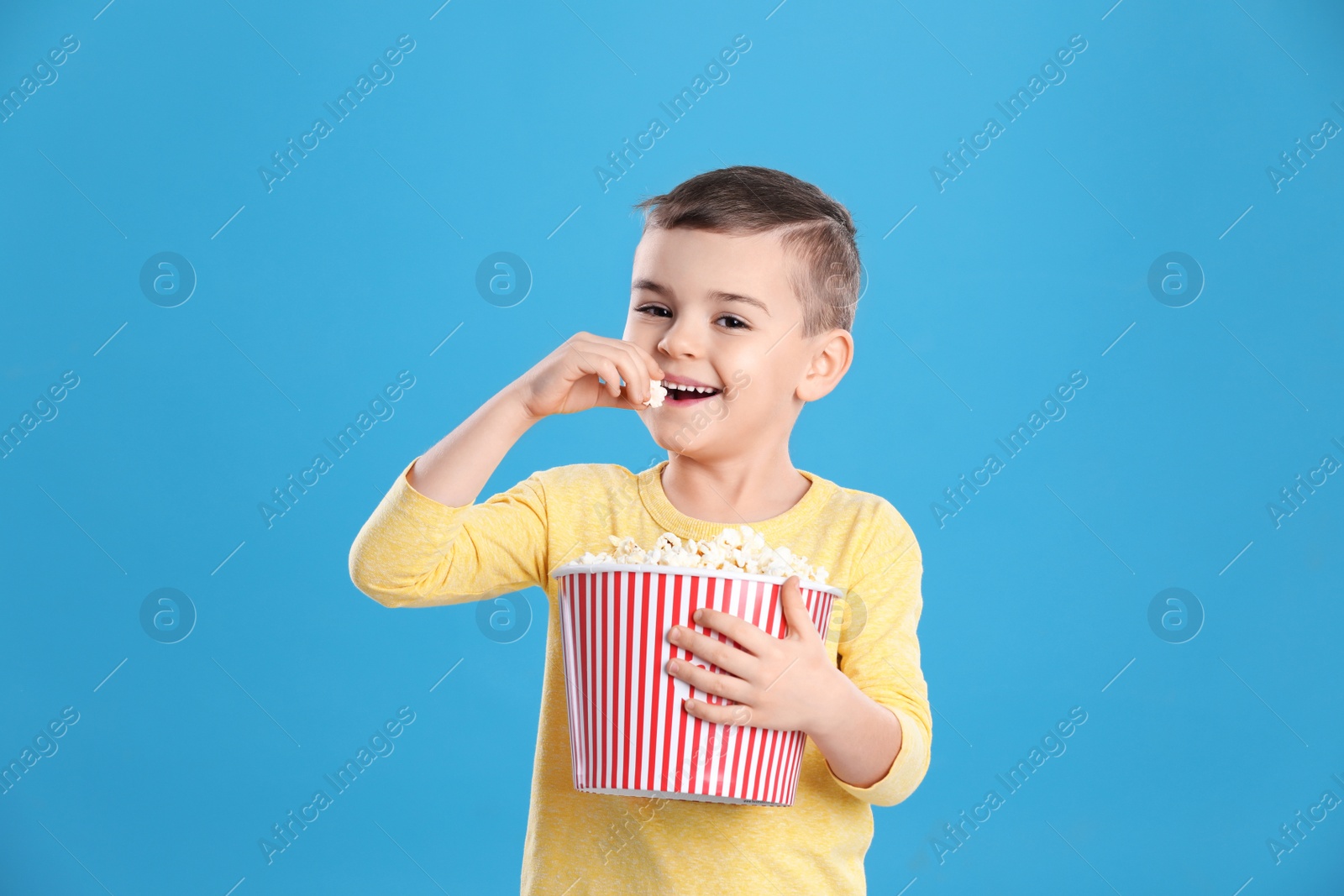 Photo of Cute little boy with popcorn on color background