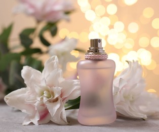 Photo of Bottle of perfume and beautiful lily flowers on table against beige background with blurred lights, closeup