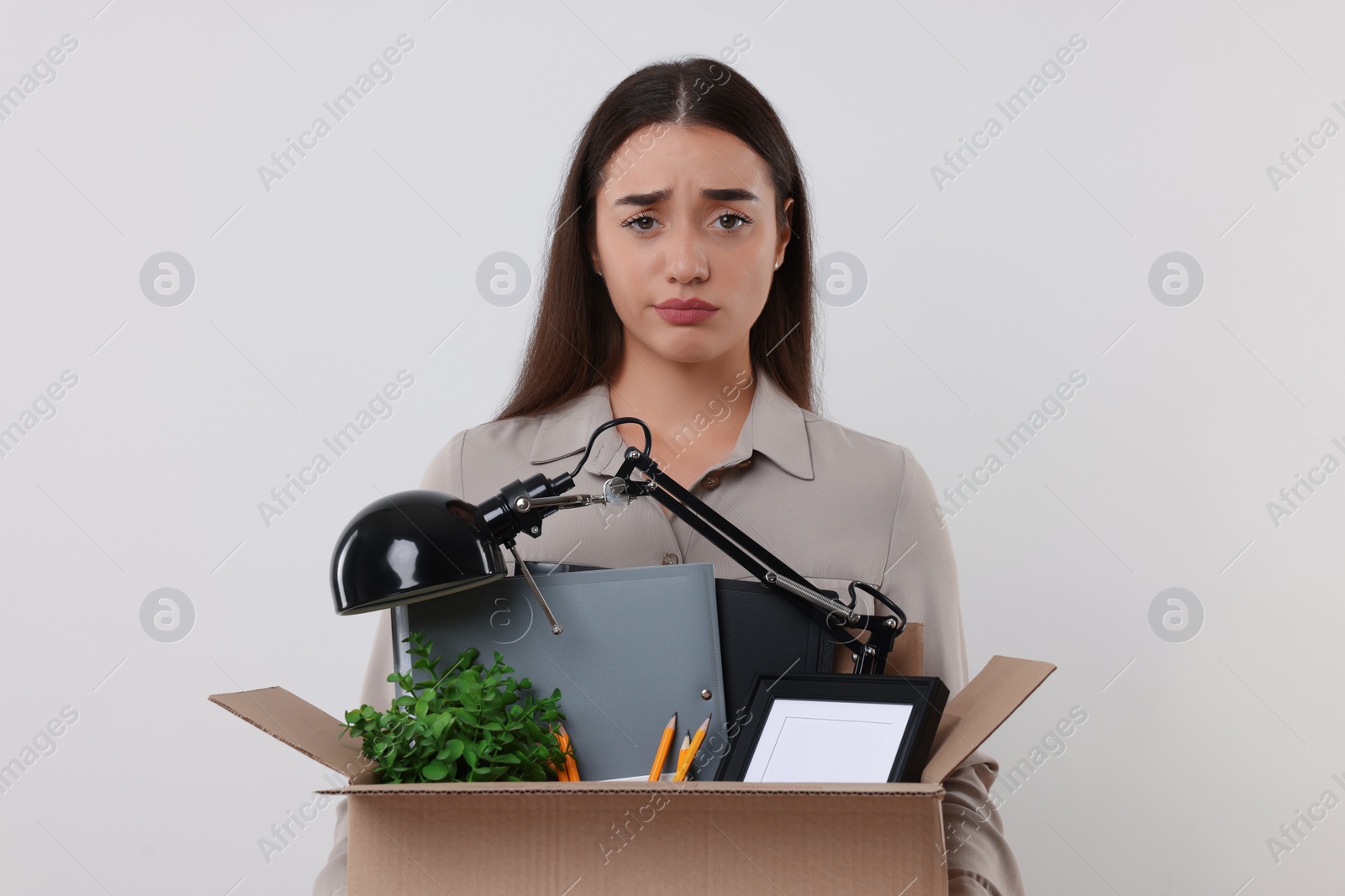 Photo of Unemployment problem. Unhappy woman with box of personal office belongings on white background