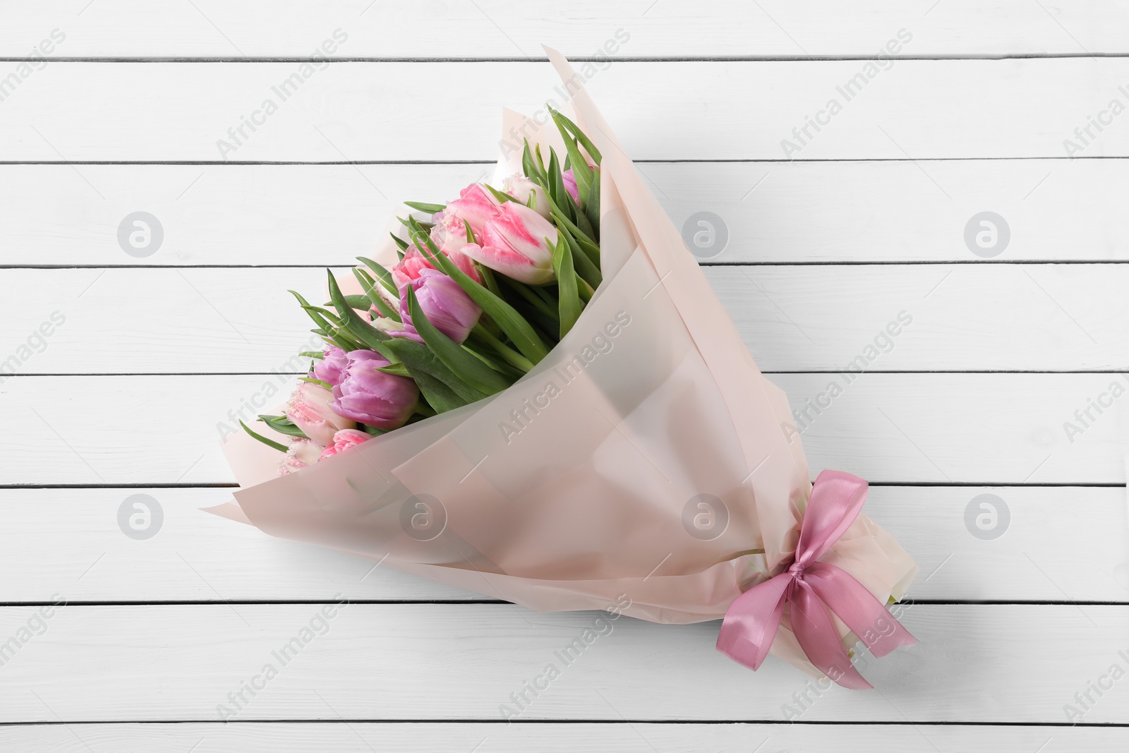 Photo of Bouquet of beautiful tulips on white wooden table, top view