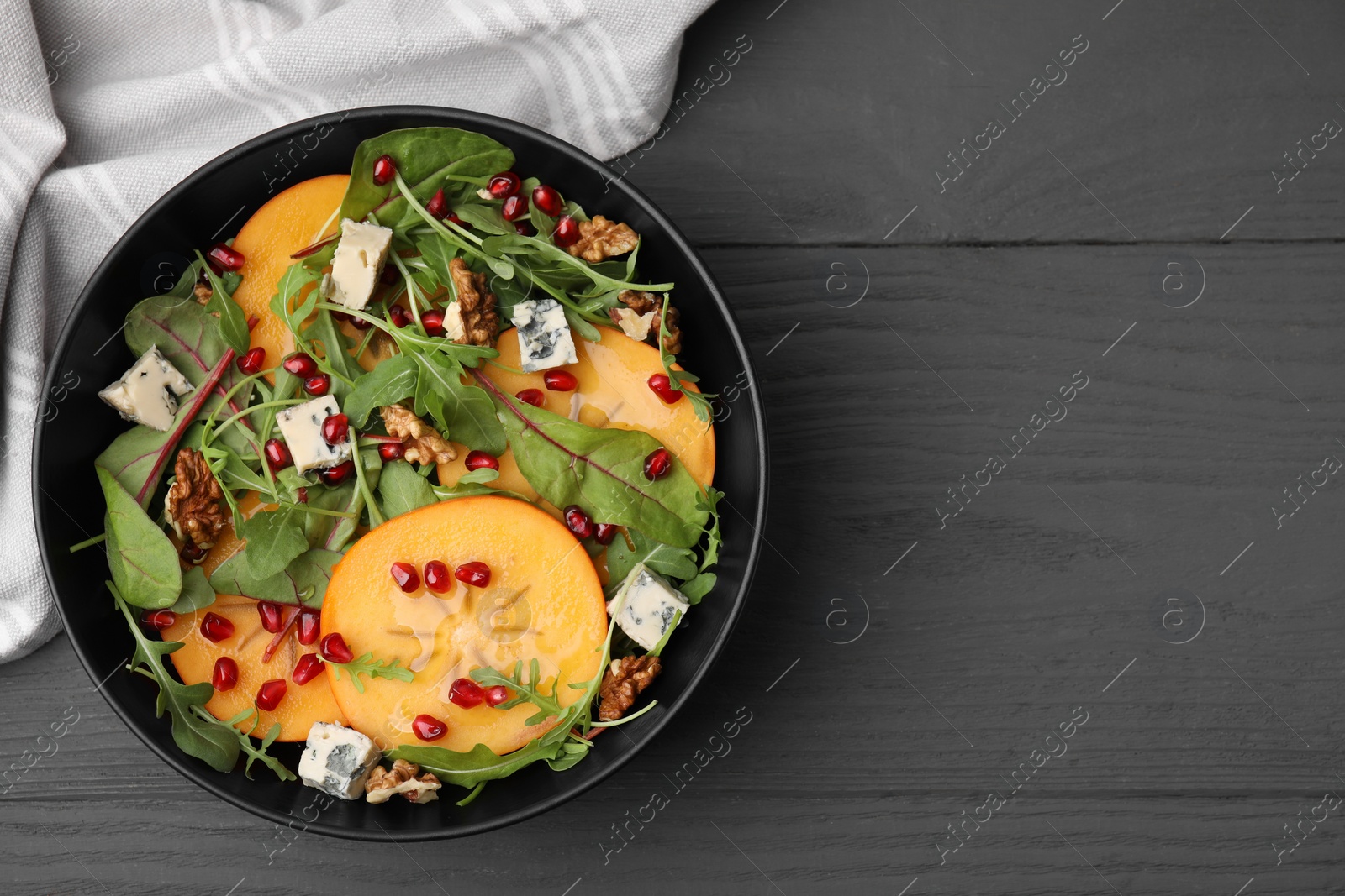 Photo of Tasty salad with persimmon, blue cheese, pomegranate and walnuts served on grey wooden table, top view. Space for text