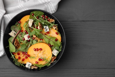 Photo of Tasty salad with persimmon, blue cheese, pomegranate and walnuts served on grey wooden table, top view. Space for text