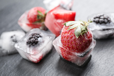 Ice cubes with different berries on dark grey table, closeup