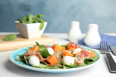 Photo of Fresh melon with prosciutto, mozzarella and arugula on white wooden table