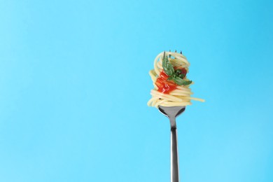 Photo of Fork with tasty pasta, basil and tomato sauce on light blue background, space for text