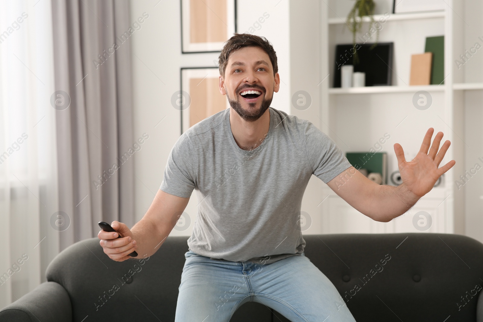 Photo of Emotional man holding remote controller and watching TV at home