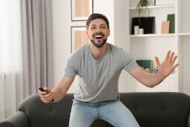 Emotional man holding remote controller and watching TV at home