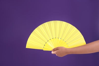 Photo of Woman holding yellow hand fan on purple background, closeup