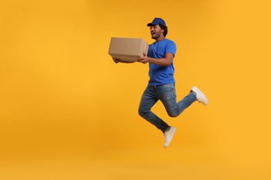 Photo of Happy courier with parcel jumping on orange background, space for text
