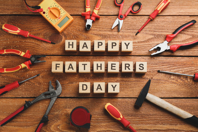 Photo of Wooden cubes with phrase HAPPY FATHER'S DAY and different tools on wooden background, flat lay