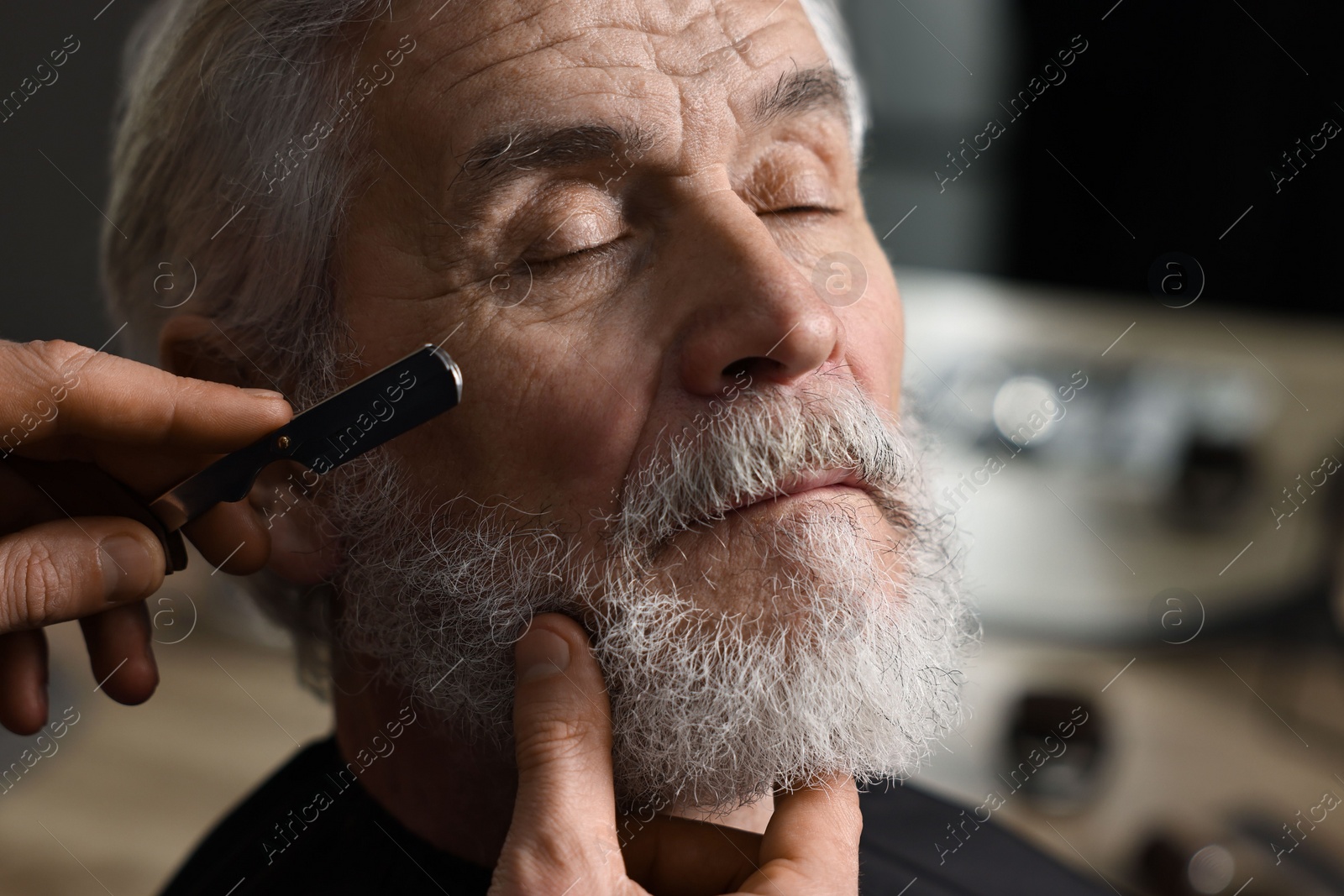 Photo of Professional barber shaving client's beard with blade in barbershop