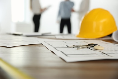 Photo of Colleagues in office, focus on table with construction drawings and tools