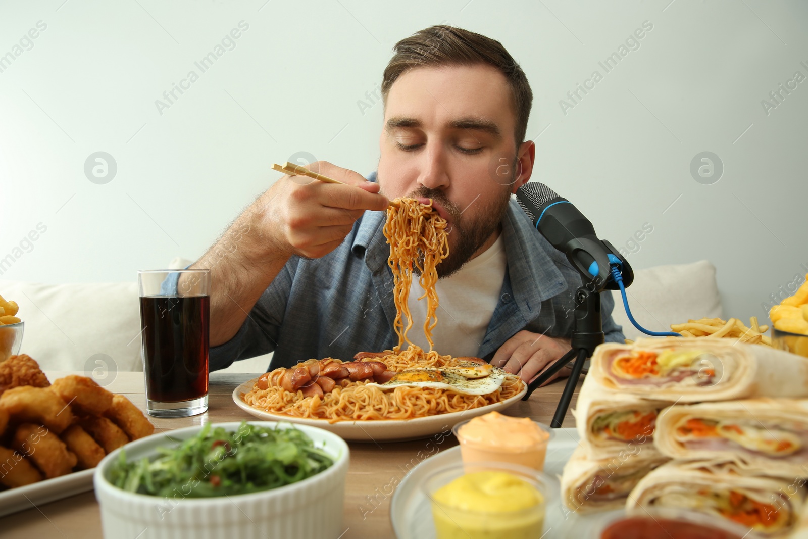 Photo of Food blogger eating in front of microphone at table against light background. Mukbang vlog