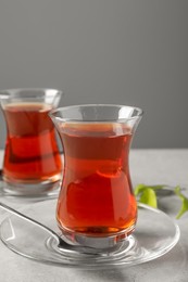 Photo of Glasses with traditional Turkish tea and green leaves on light grey table