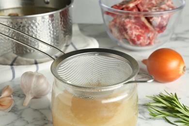 Photo of Straining delicious broth through sieve on white marble table, closeup