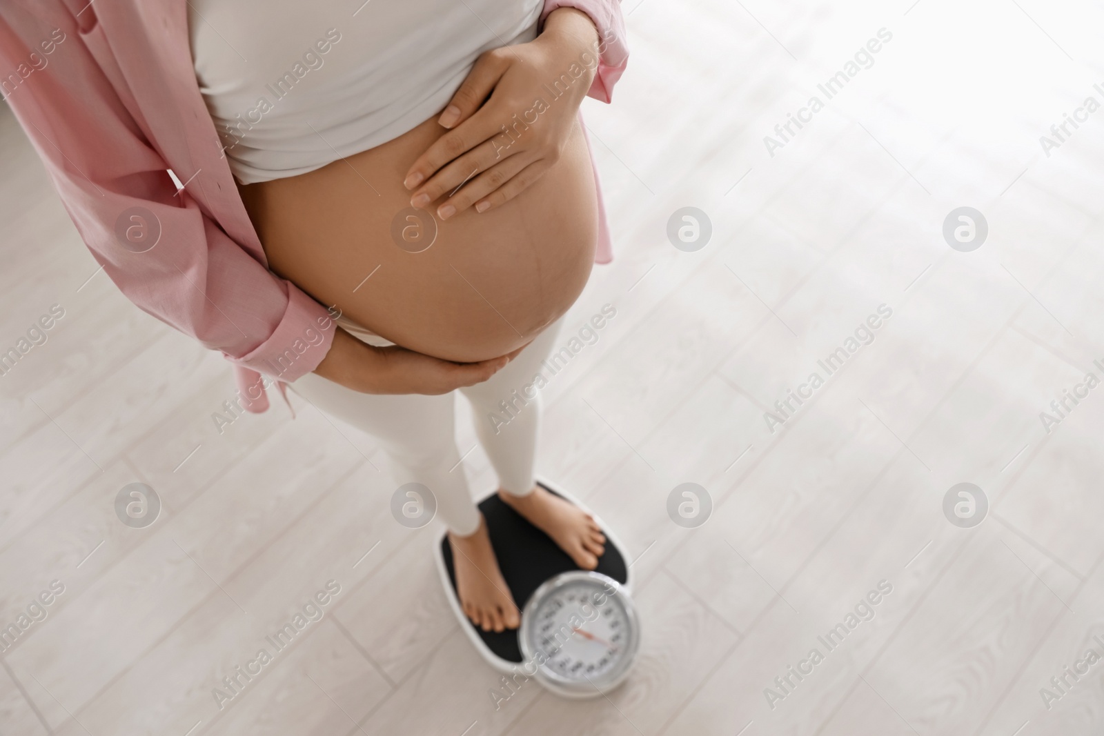 Photo of Pregnant woman standing on scales indoors, above view. Space for text