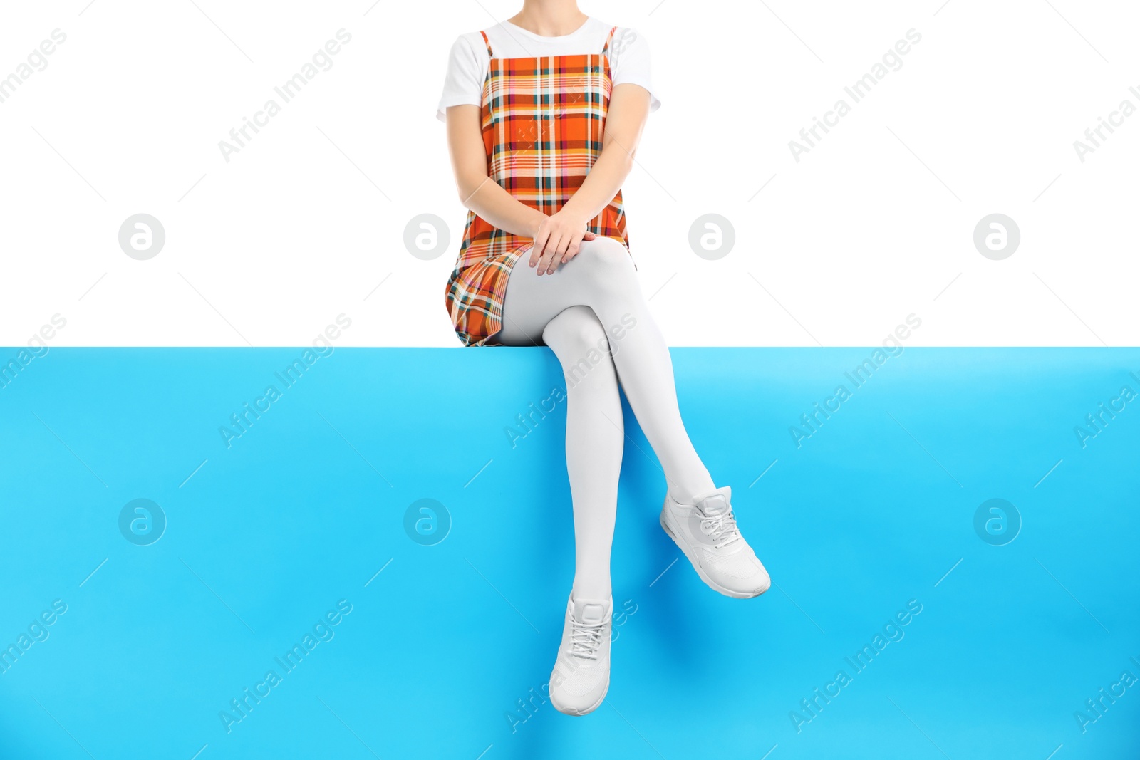 Photo of Woman wearing white tights and stylish shoes sitting on color background, closeup