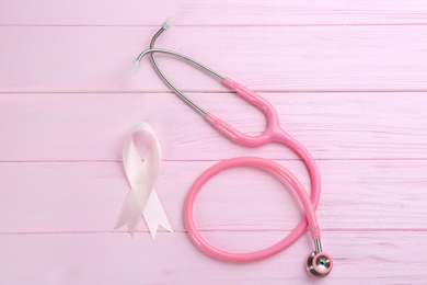 Photo of Pink ribbon and stethoscope on wooden background, flat lay. Breast cancer concept