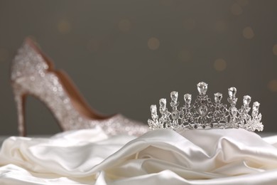 Beautiful silver tiara with diamonds near shoe on white cloth