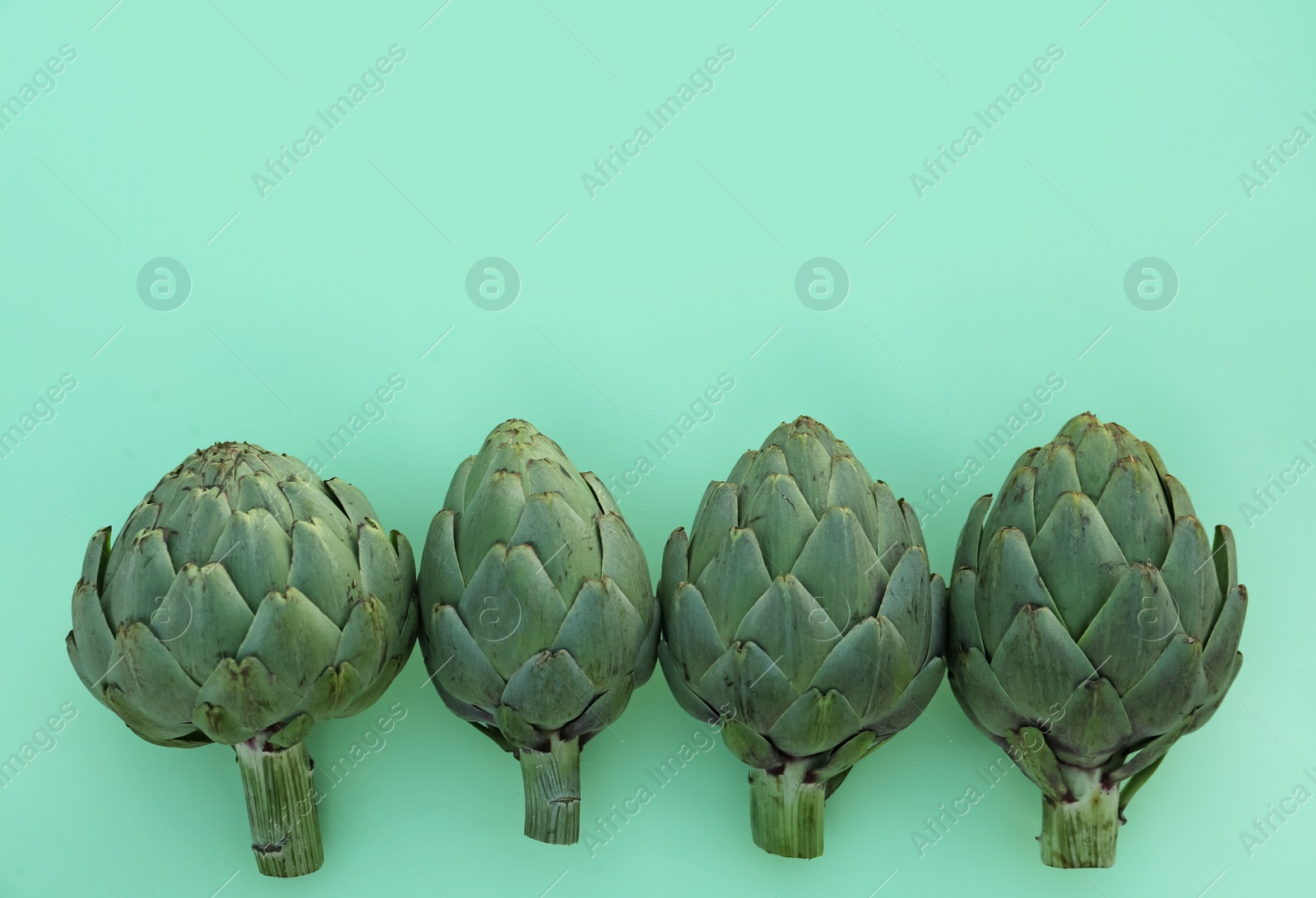 Photo of Whole fresh raw artichokes on green background, flat lay. Space for text