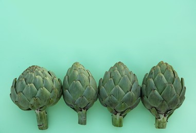 Photo of Whole fresh raw artichokes on green background, flat lay. Space for text