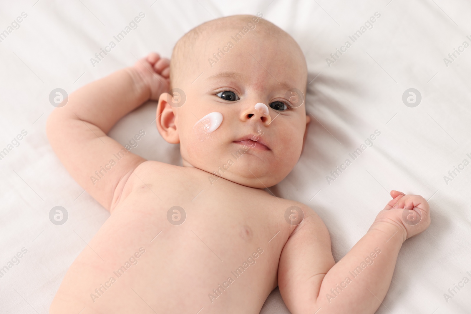 Photo of Cute little baby with cream on face on white blanket, above view