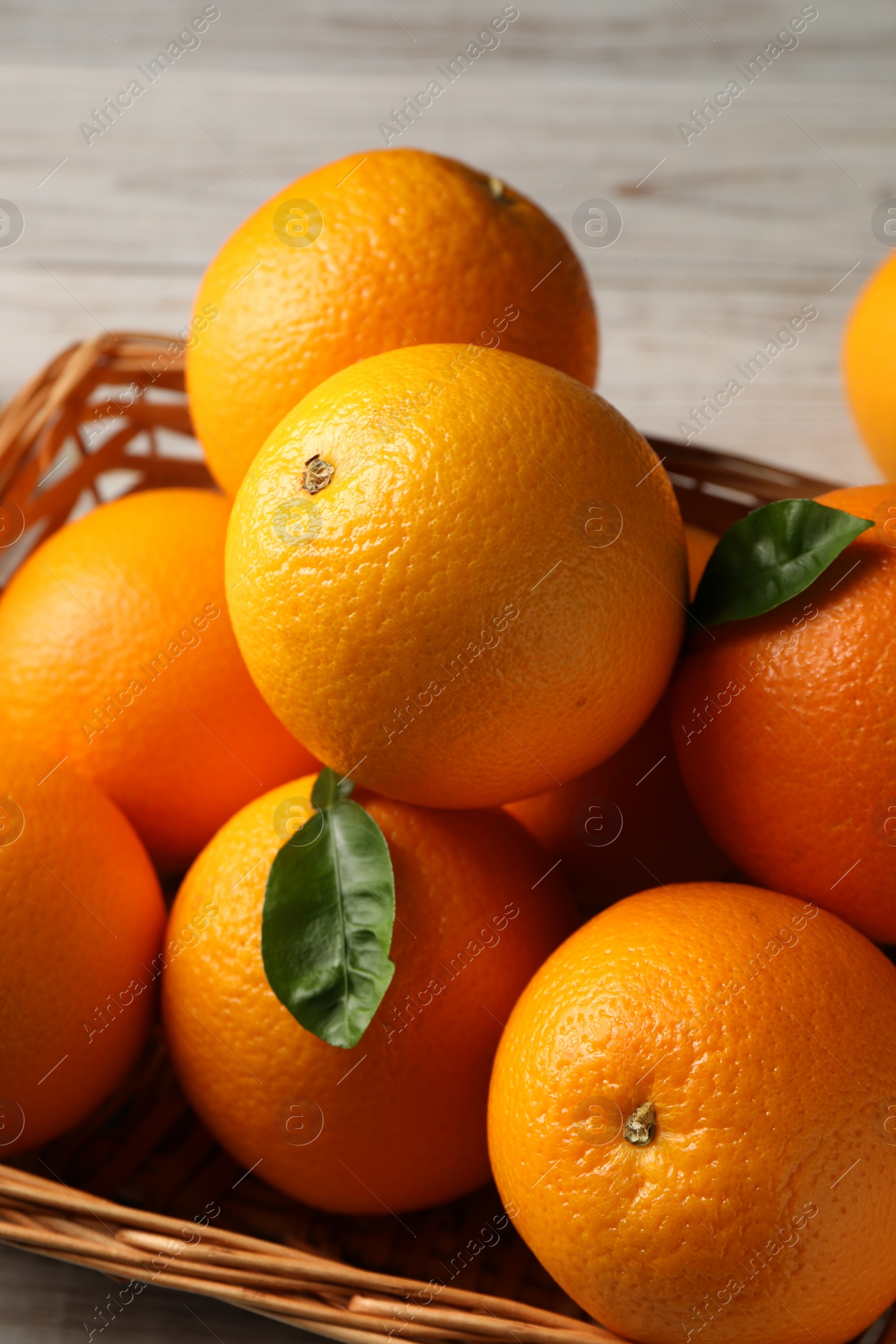 Photo of Many ripe oranges and green leaves on wooden table, closeup