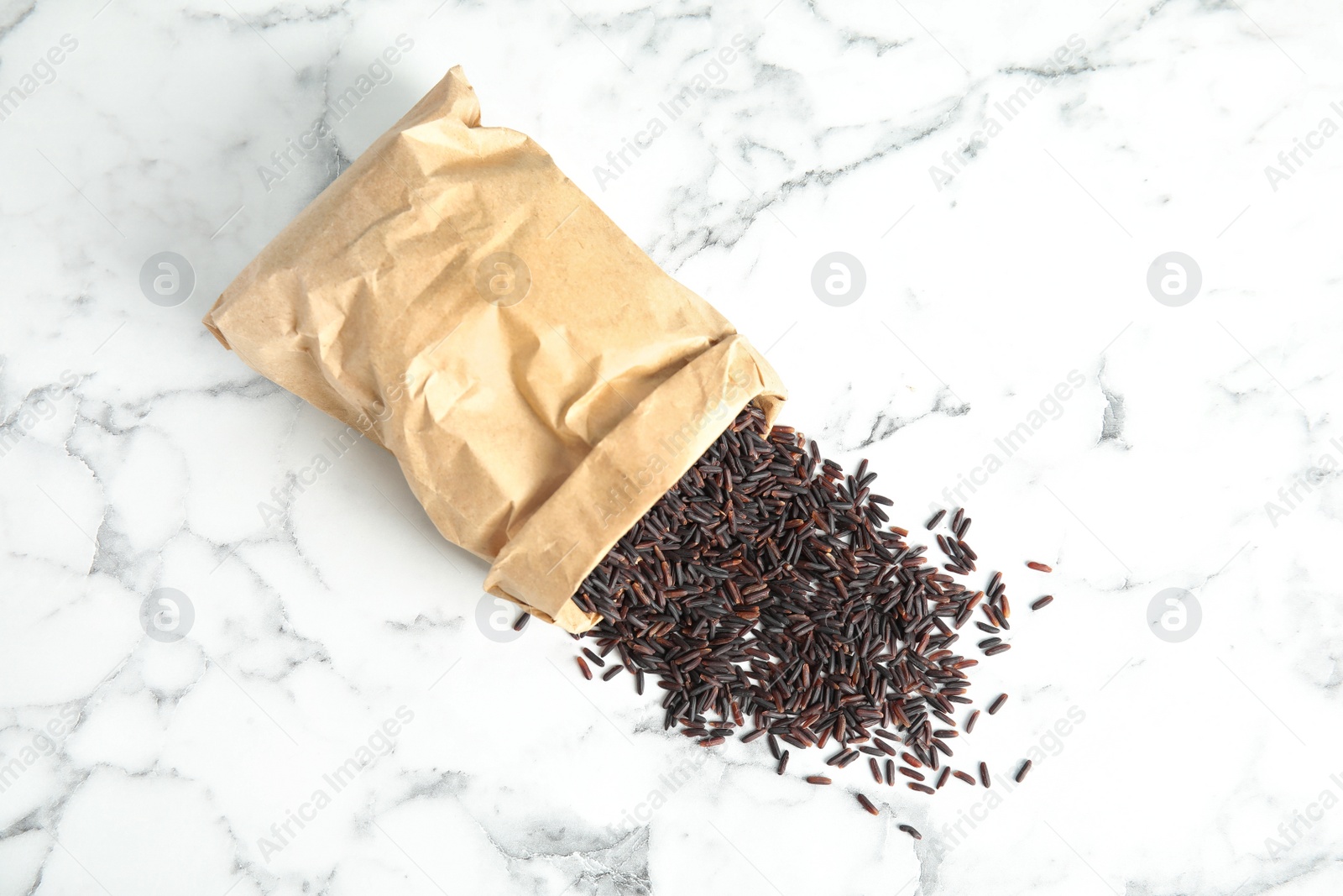 Photo of Paper bag with uncooked black rice on marble background, top view