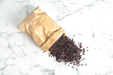 Paper bag with uncooked black rice on marble background, top view