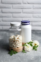 Medical bottles with pills and white flowers on light gray textured table