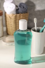 Bottle of mouthwash and toothbrushes on light table in bathroom