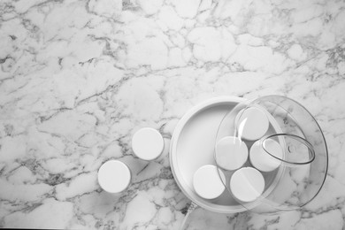 Modern yogurt maker with jars on white marble table, flat lay. Space for text