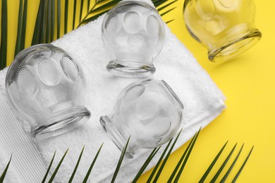 Photo of Glass cups, towel and leaves on yellow background, flat lay. Cupping therapy