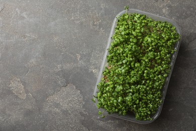 Photo of Sprouted arugula seeds in plastic container on grey table, top view. Space for text